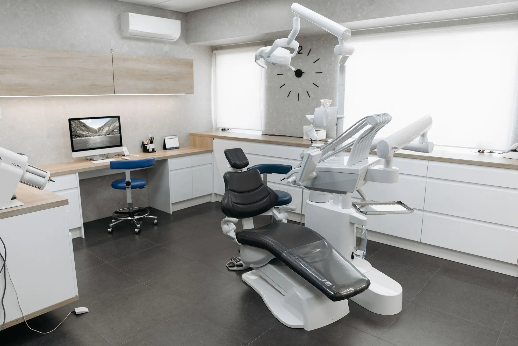 A modern dental treatment room with a reclined chair, a desk, and a large window