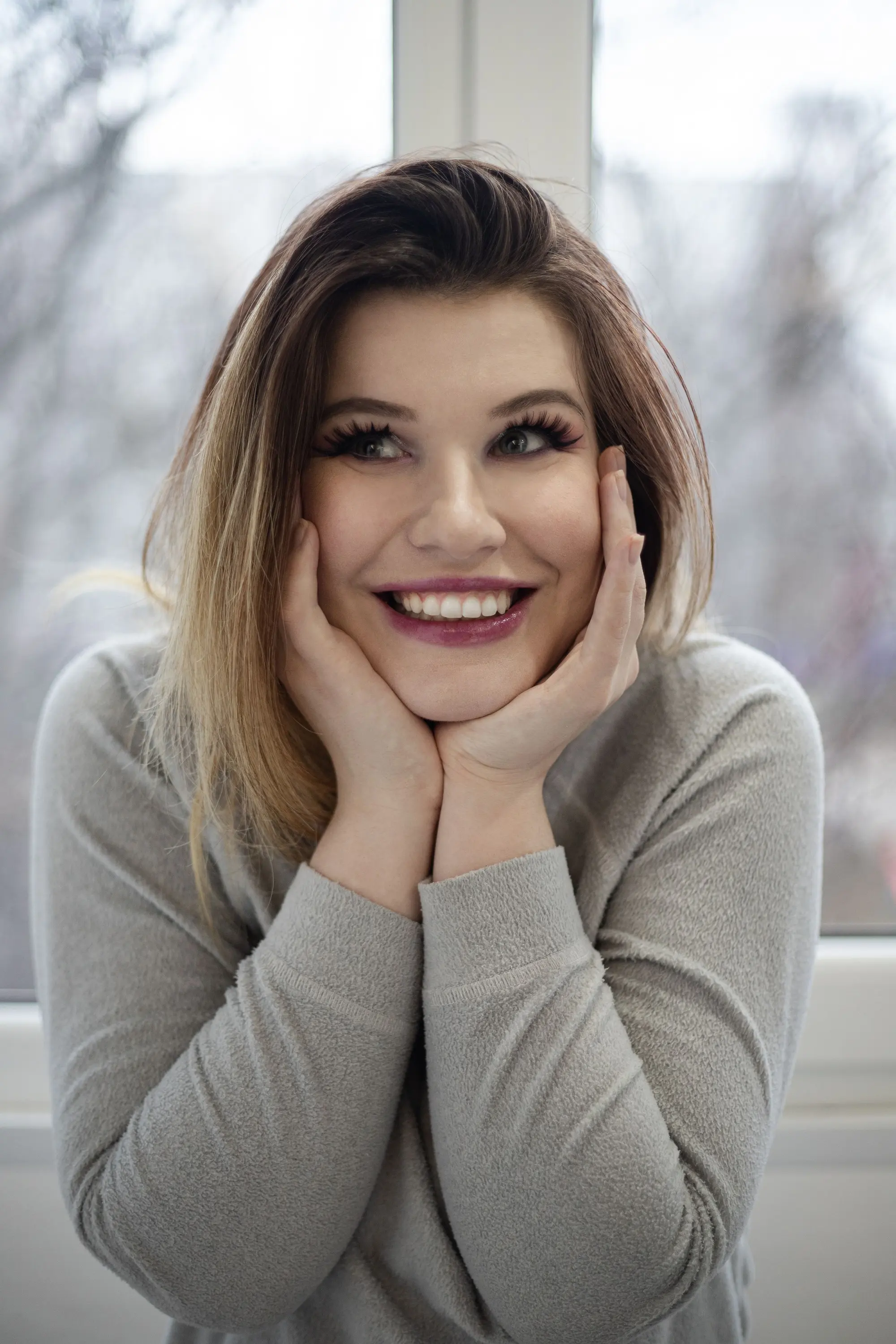 A woman with her hands under her chin, smiling warmly at the camera
