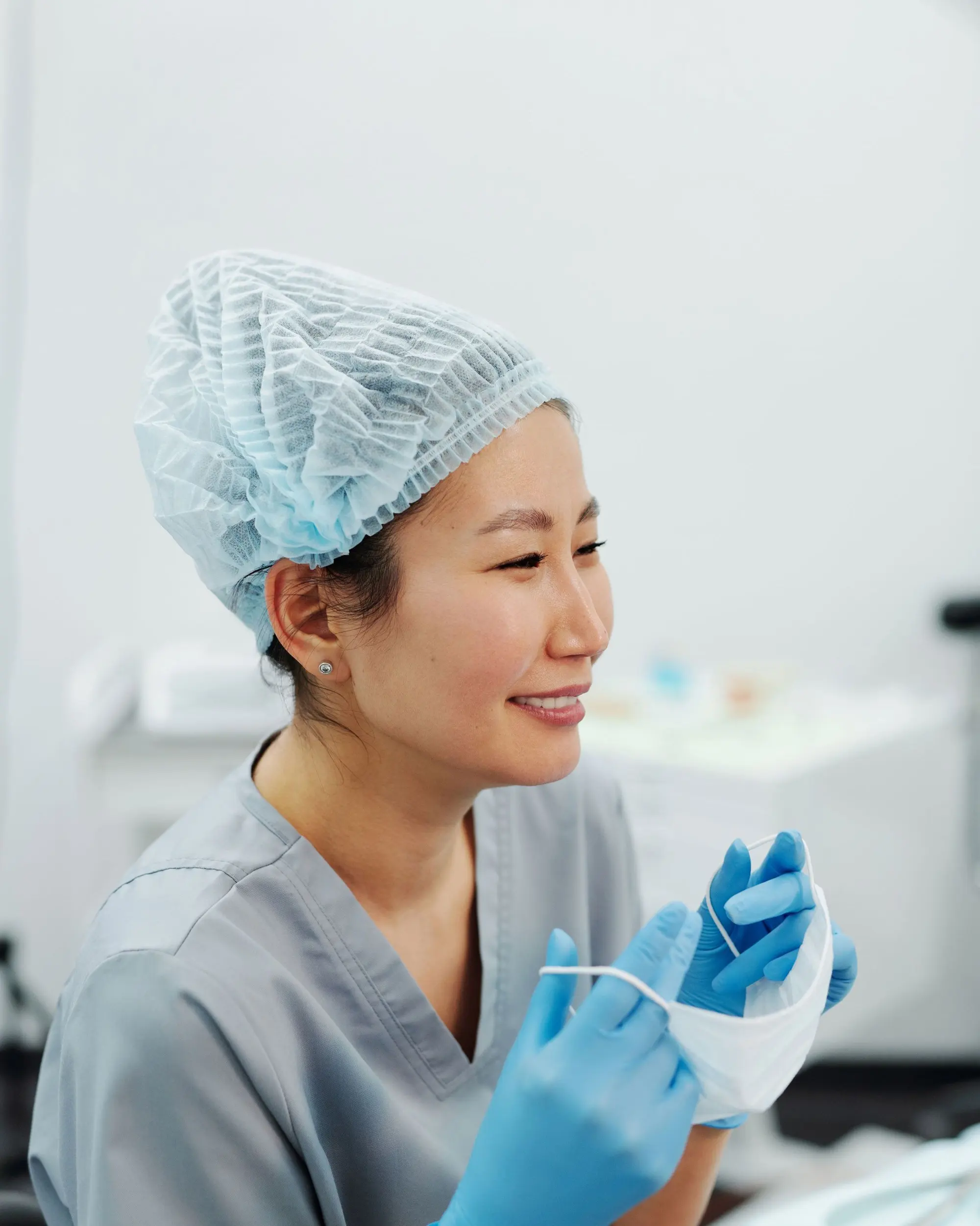 A smiling dentist in a surgical cap and grey scrubs